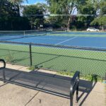 green and blue tennis courts with spectator bench